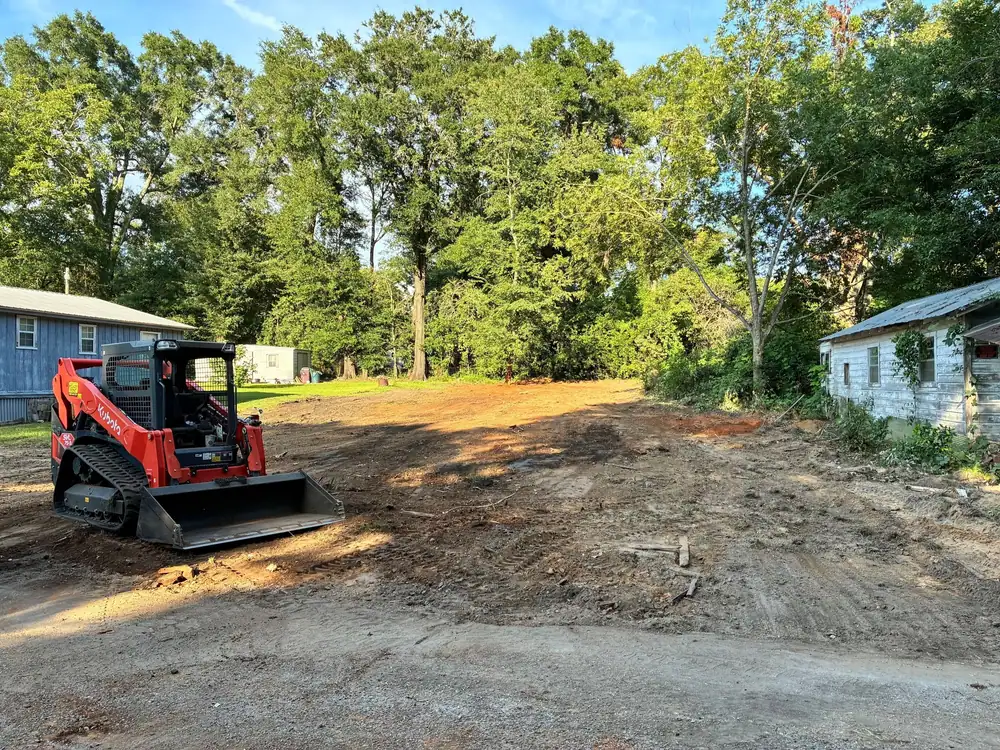 Red Kubota track loader parked on a freshly cleared and graded lot between two houses