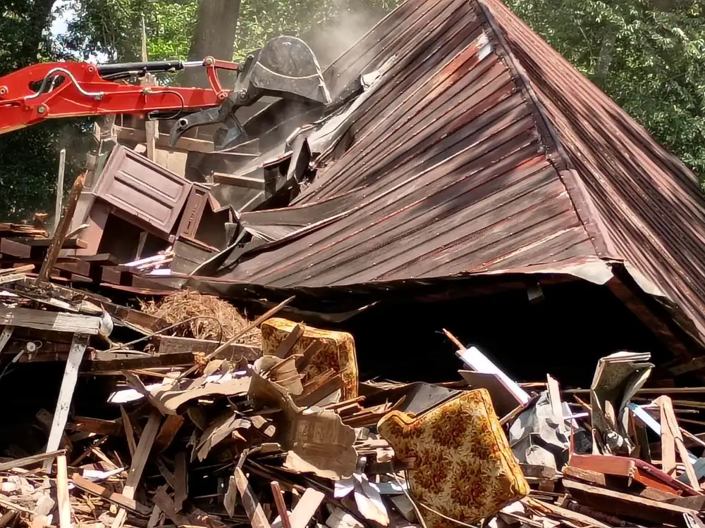 Excavator grapple pulling down a rusted metal roof during a house demolition