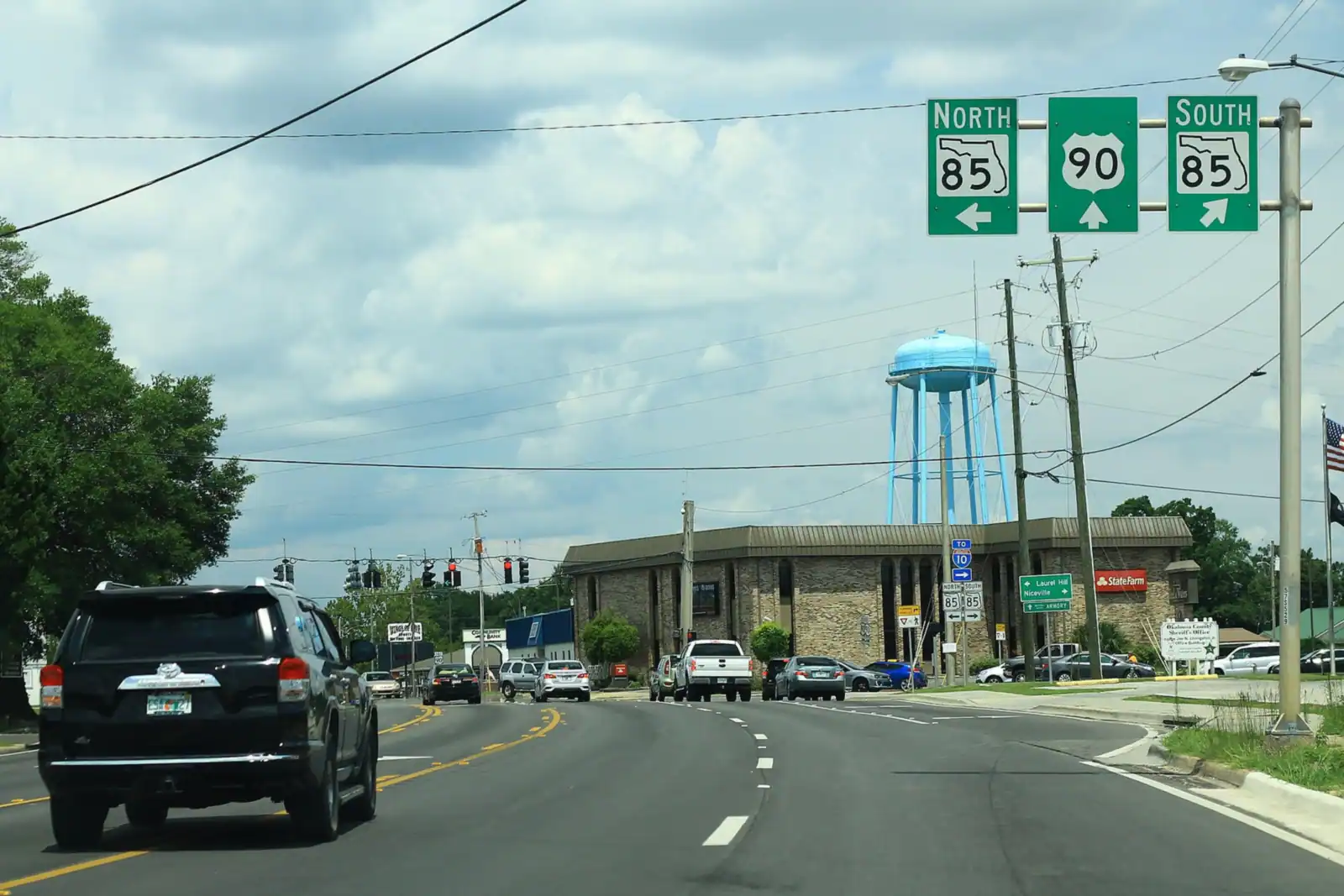 US 90 and SR 85 signs at the crossroads in Crestview, FL, with the water tower behind
